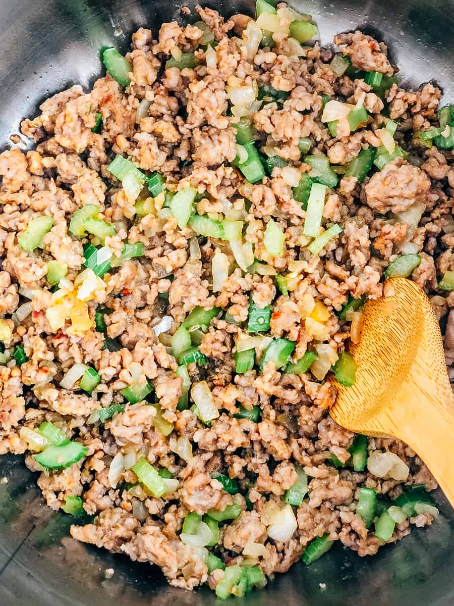 Saucisse italienne dorée, céleri et oignons au fond d'une grande casserole.