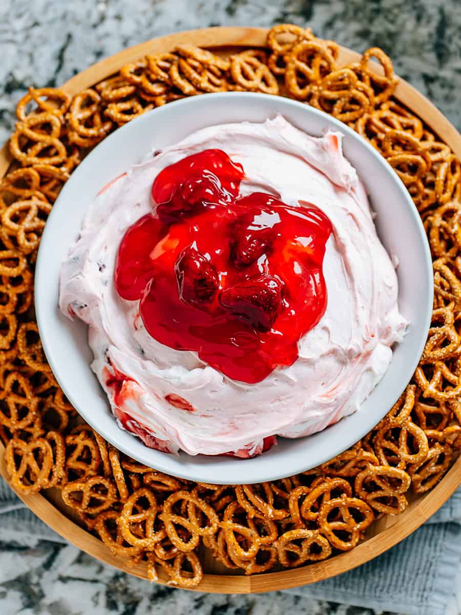 Dip de salade de bretzels à la fraise dans un grand bol de service rond avec des mini bretzels enroulés autour sur un plateau tournant.