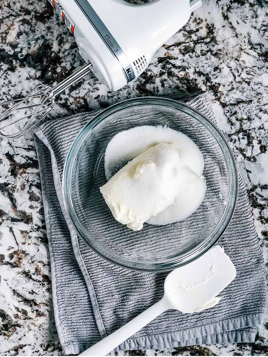 Un bol de mélange en verre moyen avec un bloc de fromage à la crème ramolli, du sucre et du sel ajoutés.