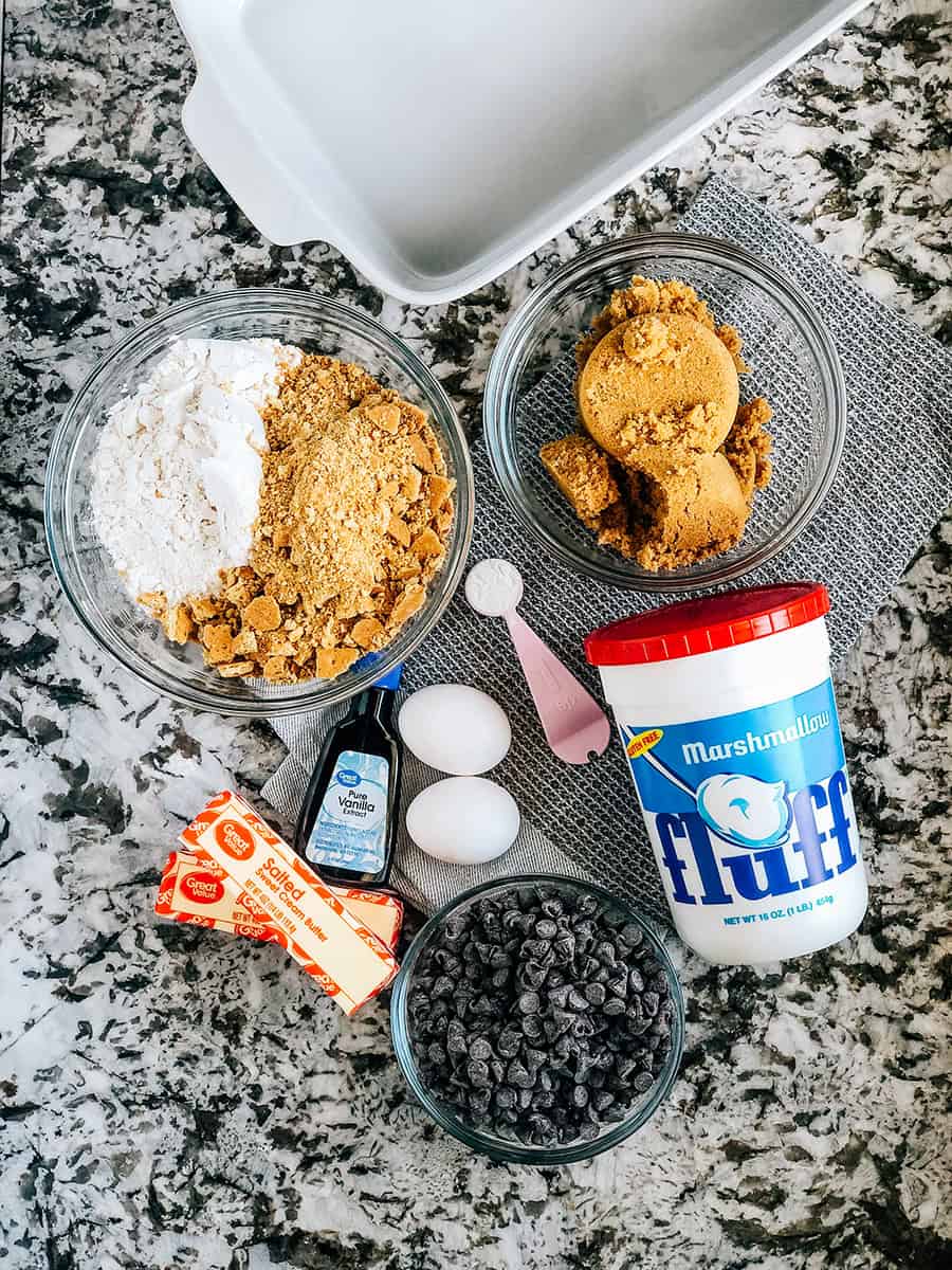 Ingrédients pour les Barres S'mores de 9x13 pouces : biscuits Graham écrasés, farine, levure chimique, œufs, vanille, beurre, sucre brun, crème de guimauve et pépites de chocolat.