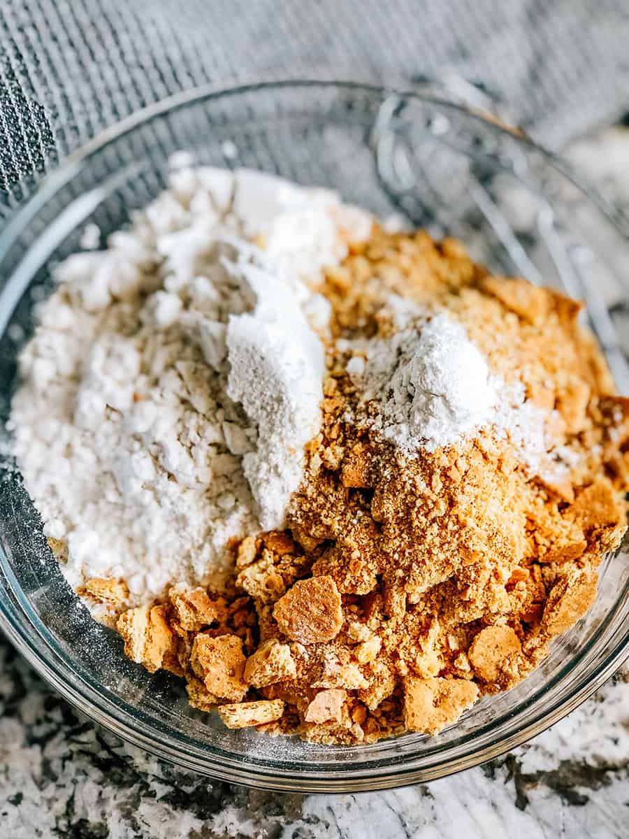 Farine, levure chimique et biscuits Graham écrasés dans un bol de mélange moyen. Les ingrédients secs pour les barres de cookies s'mores.