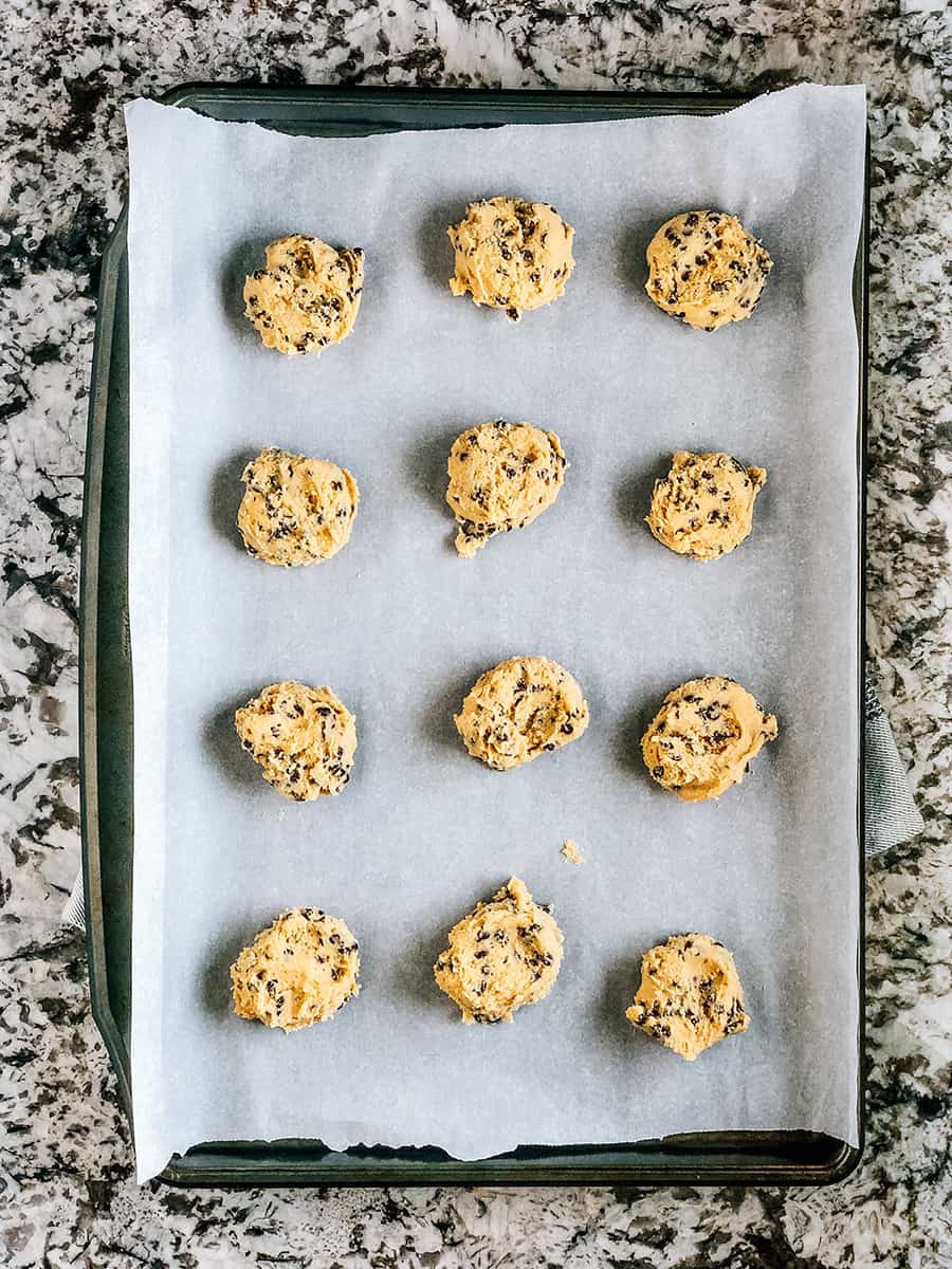 Plaque de biscuits avec des boules de pâte aplaties prêtes à être cuites.