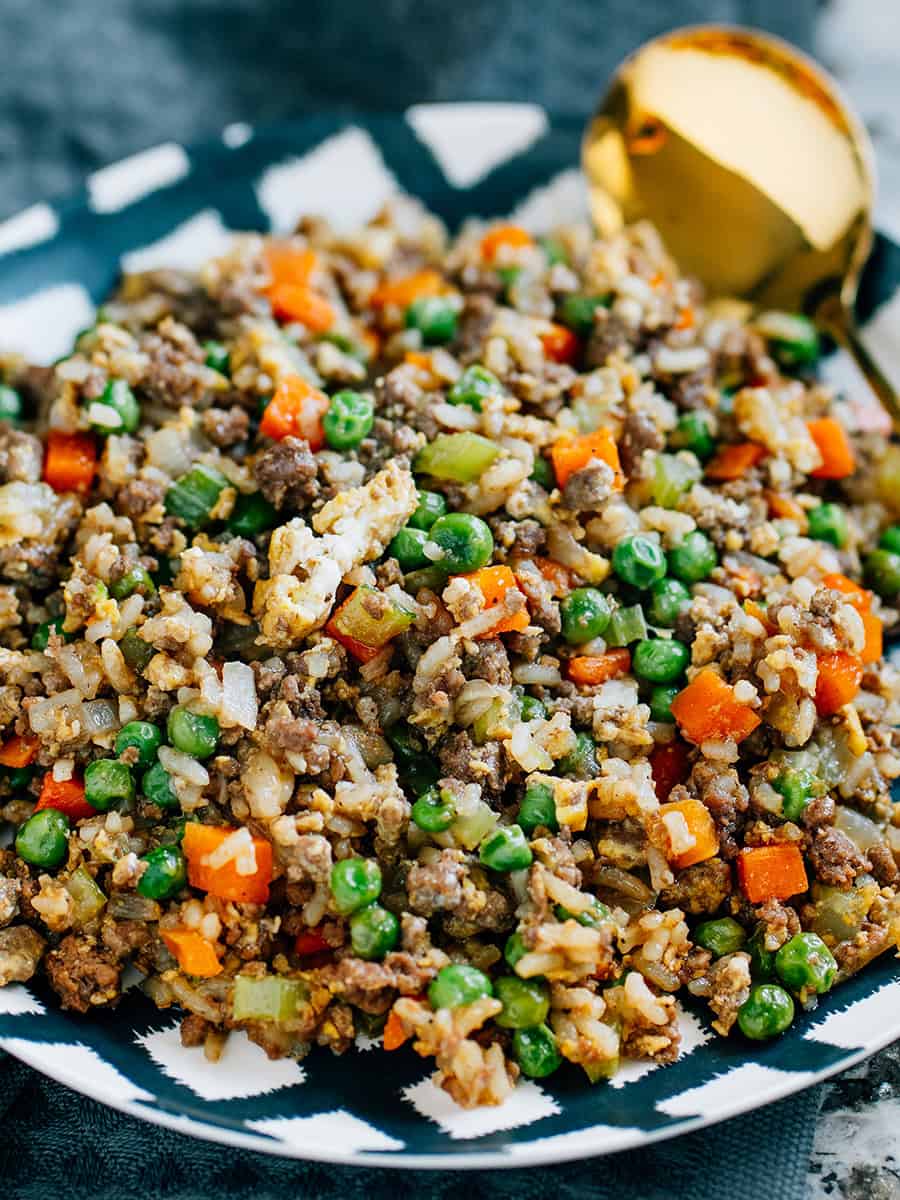 Une assiette profonde en noir et blanc remplie de bœuf haché, de riz cuit et d'œufs brouillés, tous recouverts d'une sauce soja ou d'aminos, représentant cette incroyable recette de riz frit au bœuf.