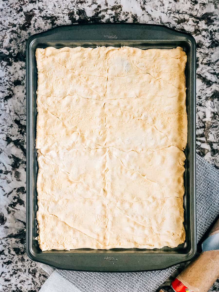 Croûte de pâte à croissant non cuite pour une pizza légumes étalée et pincée.