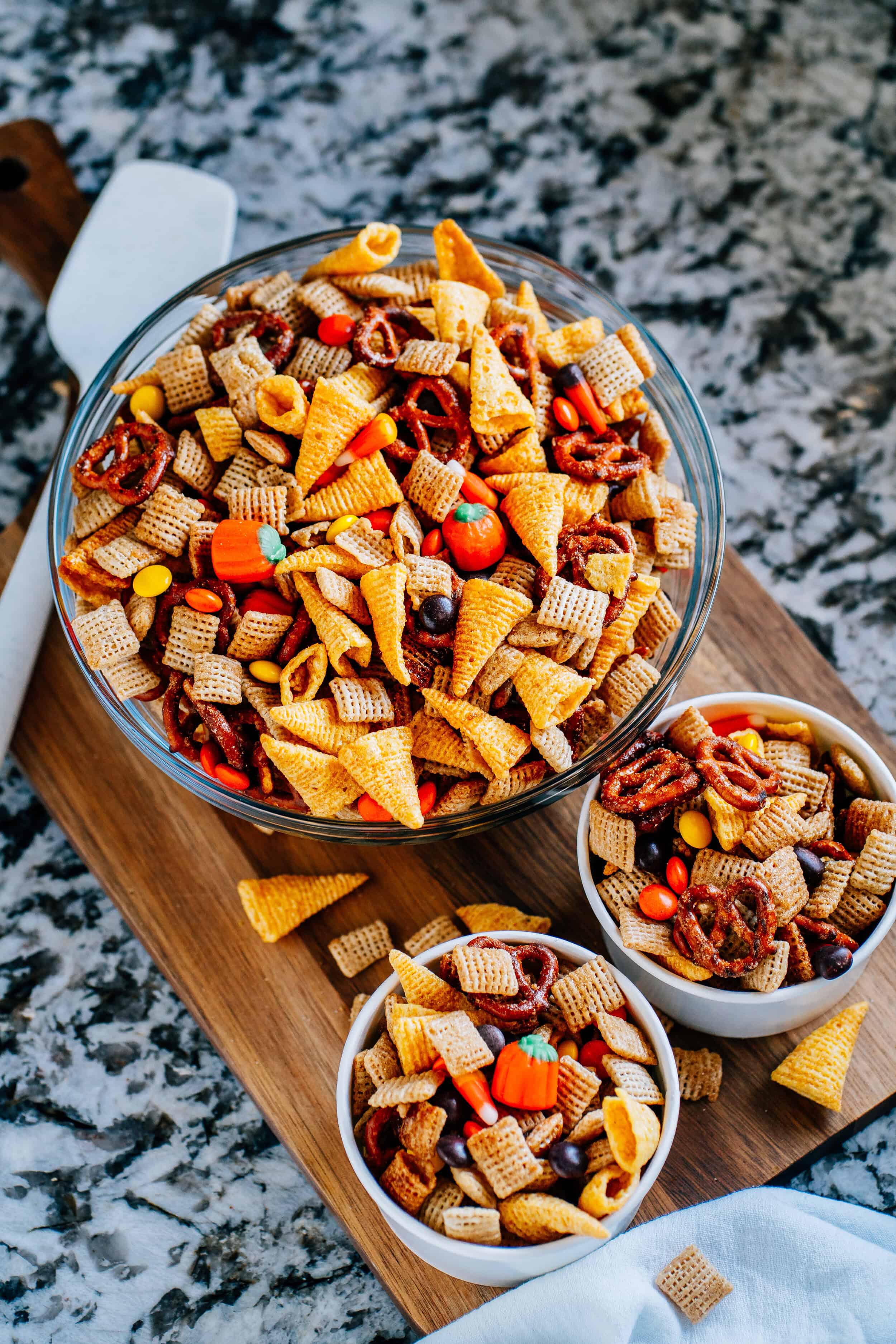 Simple, sweet and salty fall party mix with rice squares, Bugles, pretzel twists, candy corn, candy pumpkins, and Reese's Pieces in a single serving size paper cup.