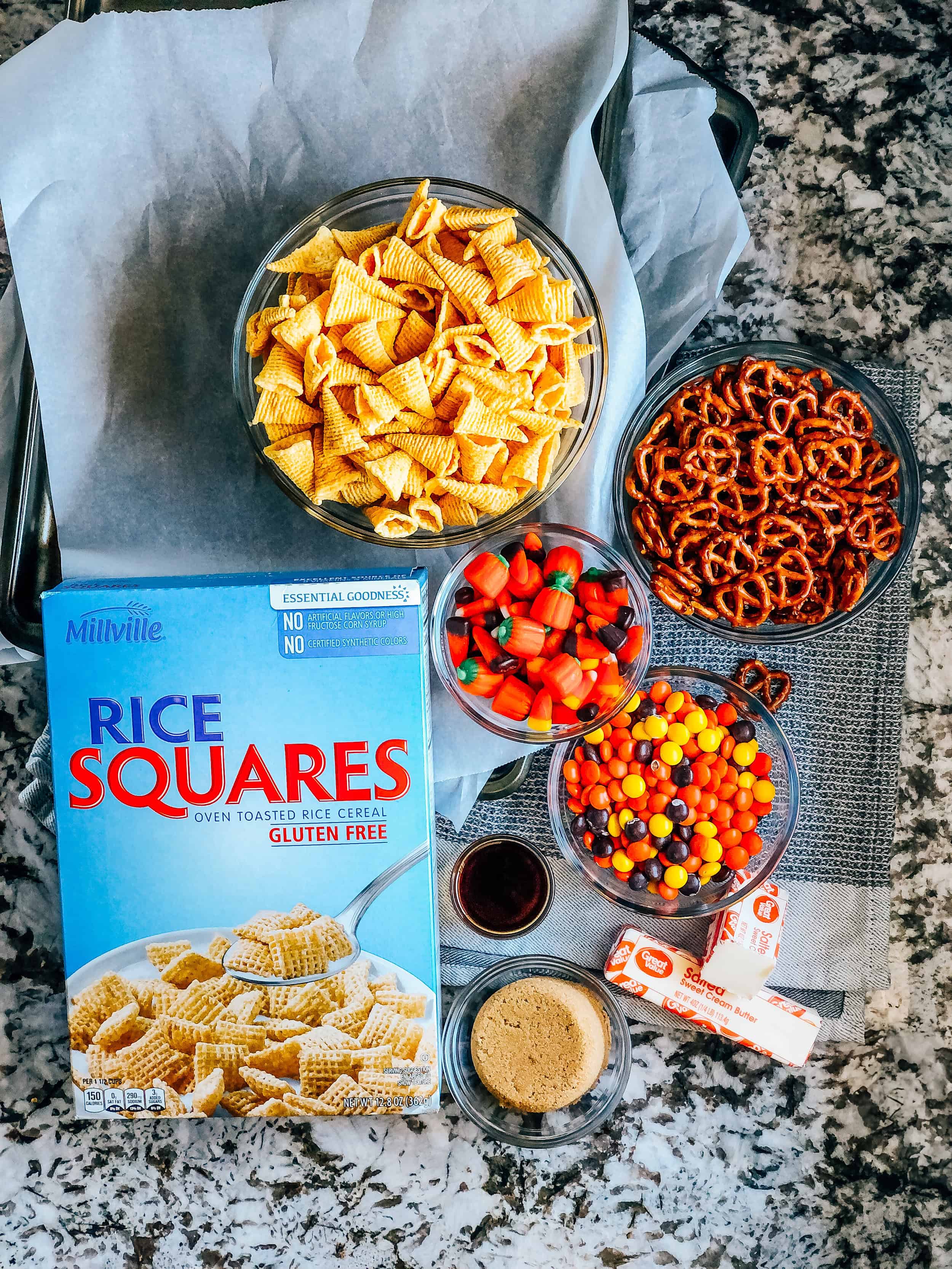 Ingredients to simple fall snack mix: box of rice squares, bag of Bugles, mini pretzel twists, candy pumpkins, candy corn, Reese's Pieces, butter, brown sugar, and vanilla.