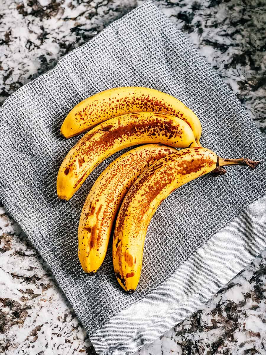 Quatre bananes très mûres sur un torchon de cuisine.