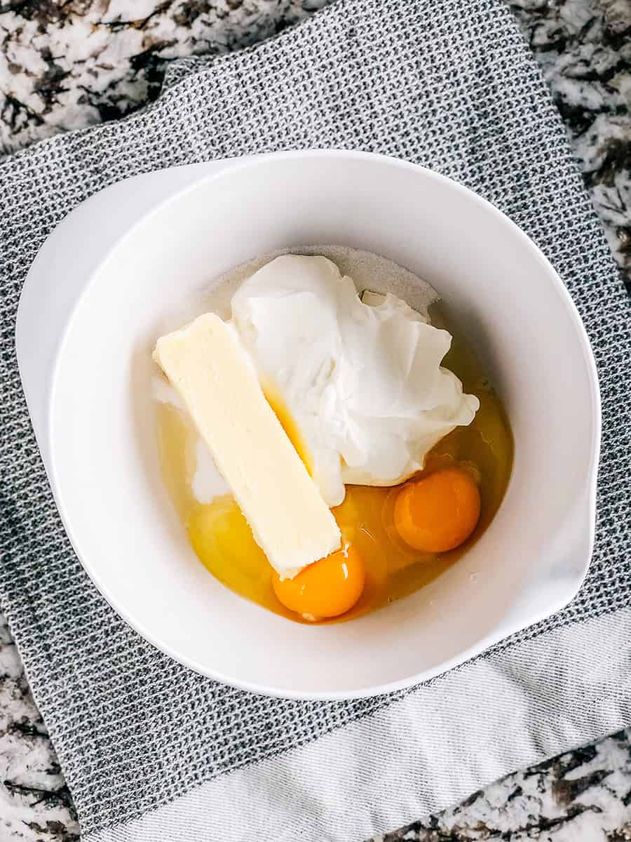 Sucre, crème aigre, beurre ramolli et œufs dans un bol de mélange.