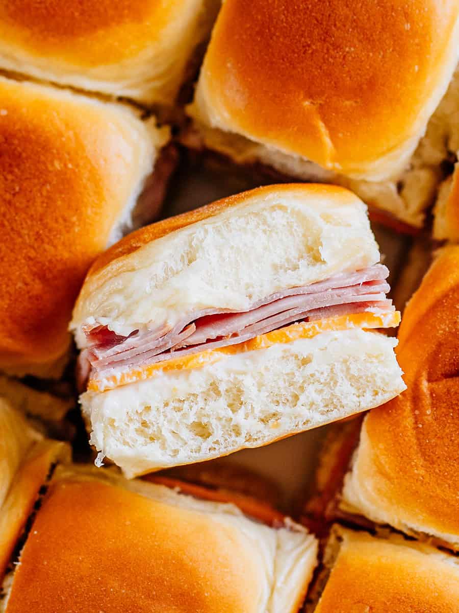 Un mini-burger froid au jambon et au fromage sur le côté entouré d'autres mini-burgers dressés.