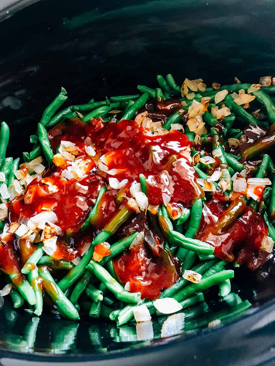 La sauce BBQ, le bacon et les oignons sur le dessus de la couche de haricots verts dans un autocuiseur.