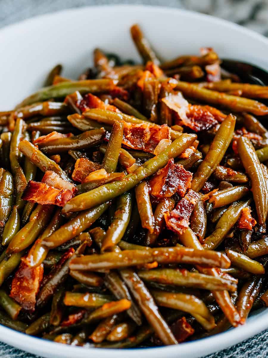 Delicieux haricots verts BBQ acides et savoureux dans un plat de service rond blanc.