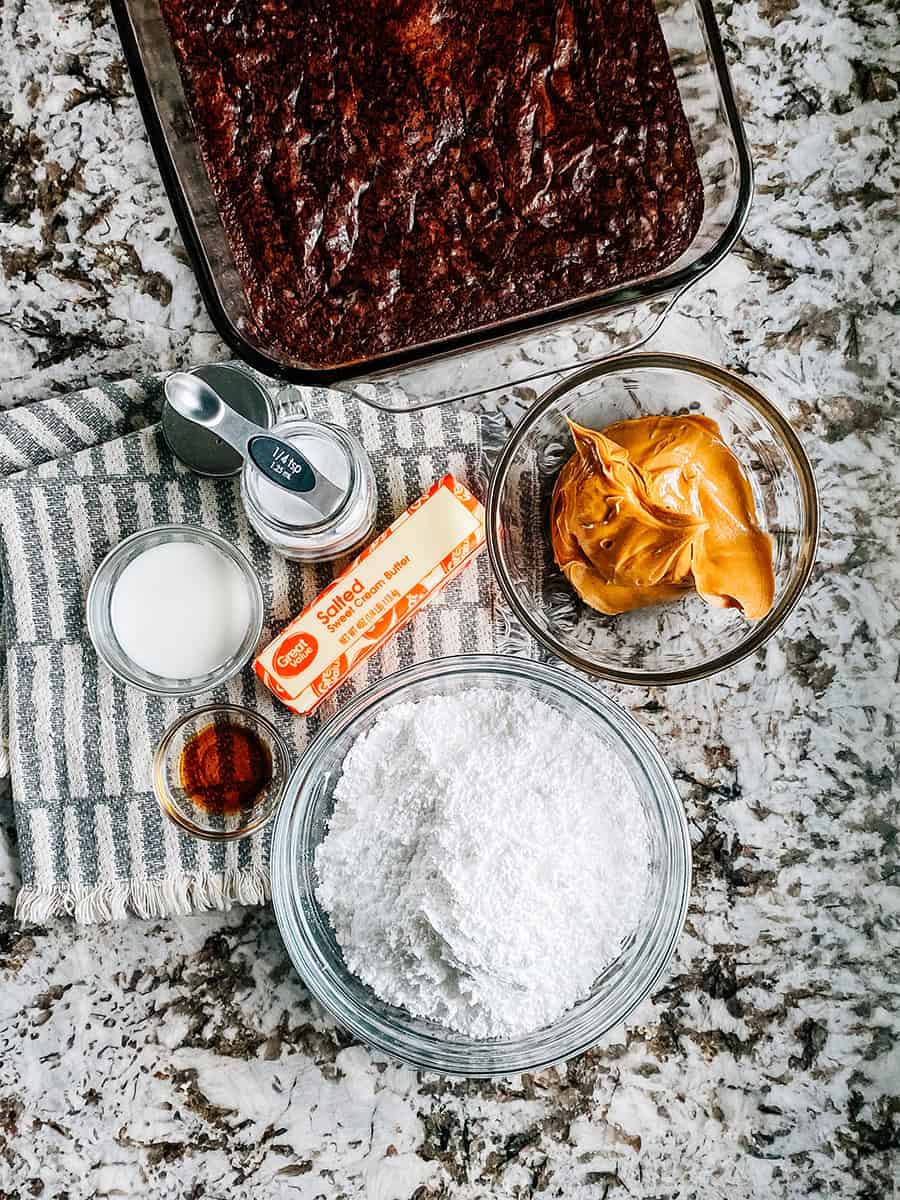 Ingrédients pour le MEILLEUR glaçage au beurre de cacahuète : un plat de brownies fraîchement cuits, du sucre glace, du beurre de cacahuète crémeux, du beurre ramolli, du sel, de l'extrait de vanille et un peu de lait !