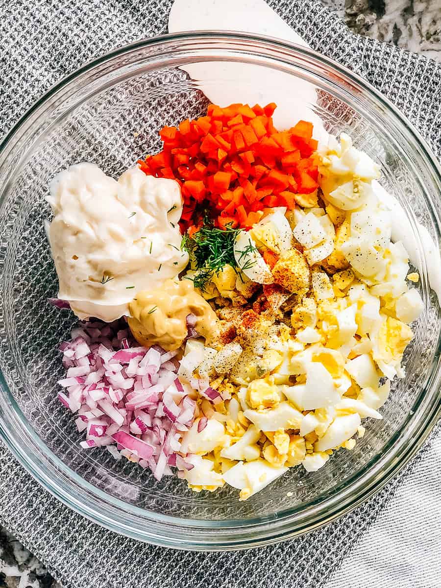 Tous les ingrédients de la salade d'œufs dans un bol en verre prêts à être mélangés pour un délicieux petit-déjeuner, déjeuner ou encas.