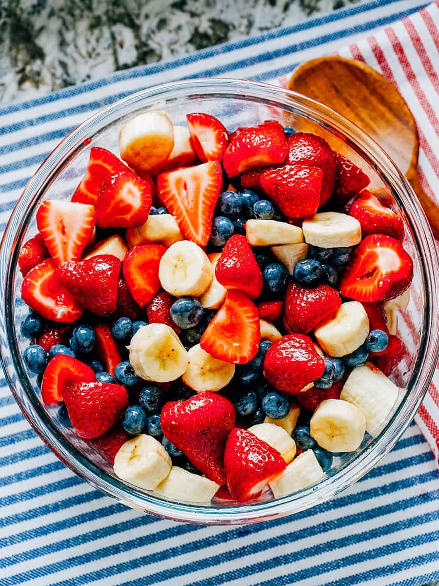 Une autre vue de fraises fraîches, bleuets et bananes enrobés de miel et de lime dans un grand bol en verre.