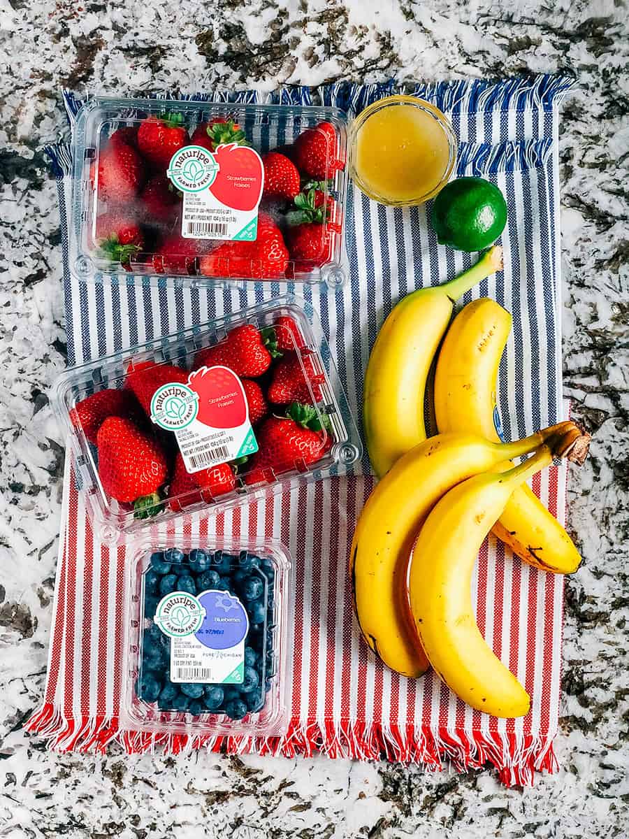 Les ingrédients d'une salade fraîche pour le 4 juillet : fraises, bleuets, bananes, jus de lime et miel.