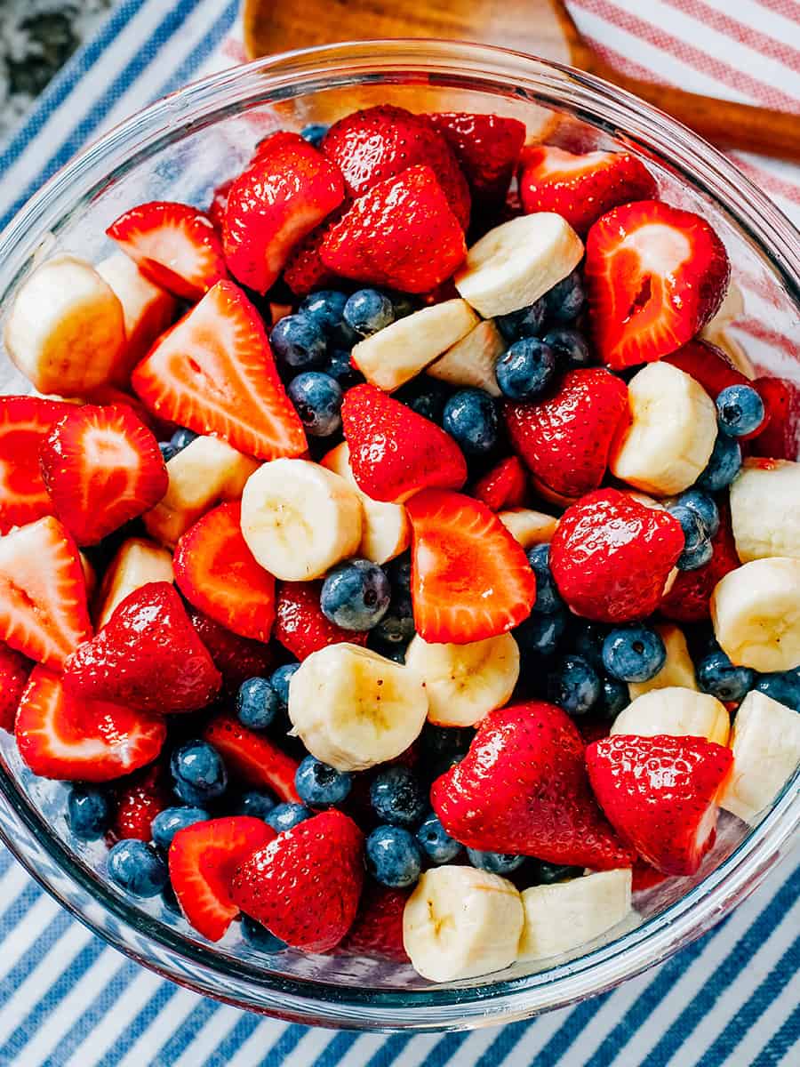 Des fraises fraîches, bleuets et bananes enrobés de miel et de lime dans un grand bol en verre.