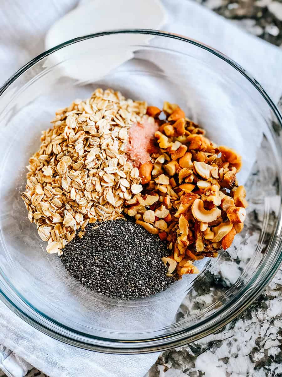 Les ingrédients secs du granola dans un bol à mélanger en verre transparent.