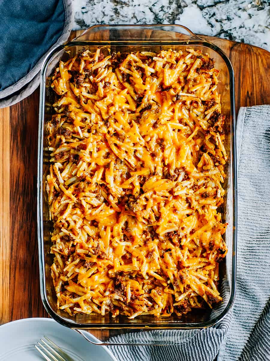 Casserole de pommes de terre rissolées à la taco chaude et fraîchement cuite sur une planche à découper en bois entourée d'assiettes et de fourchettes prêtes pour un dîner rapide et facile.