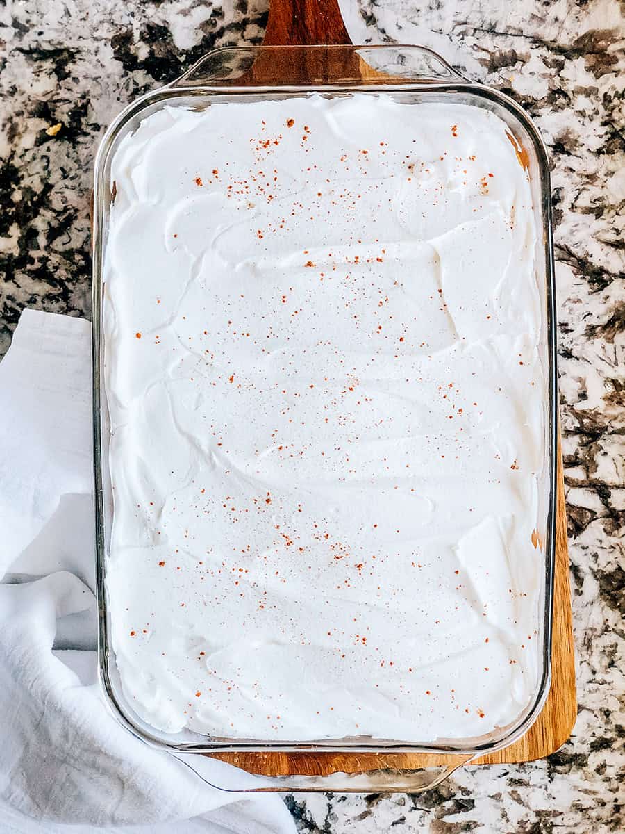 Cool whip ou topping fouetté étalé sur la garniture de tarte à la citrouille et saupoudré d'une pincée d'épices pour tarte à la citrouille.