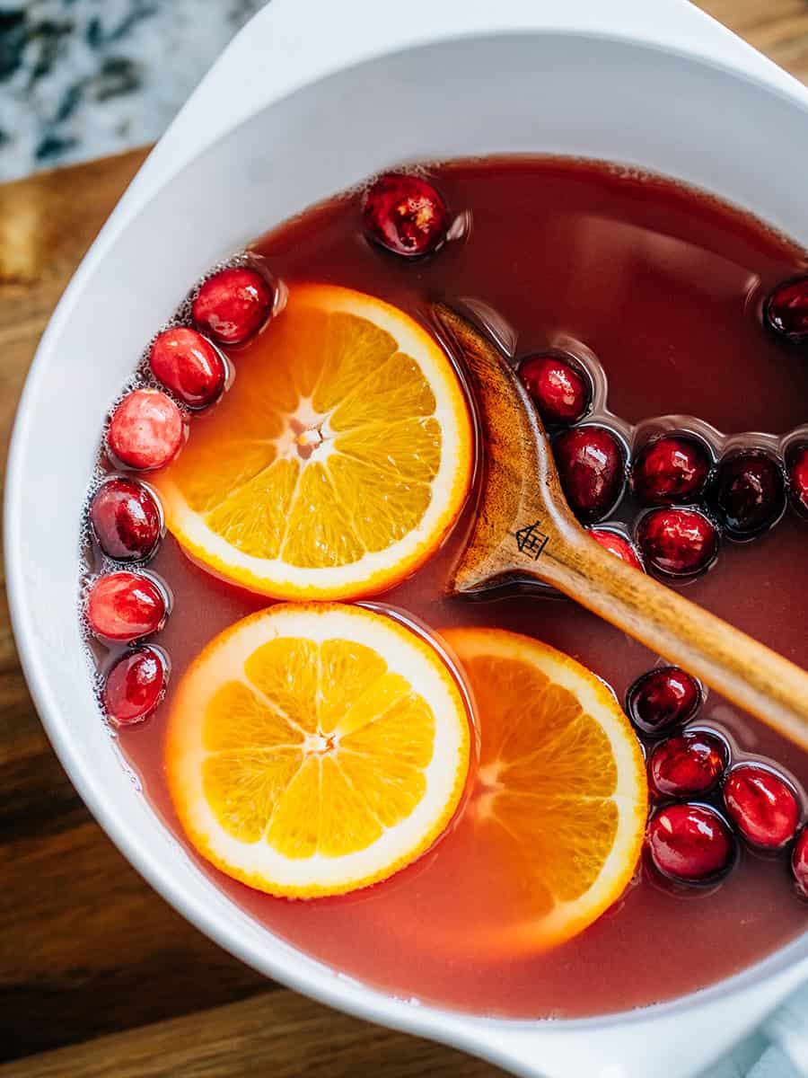 Un bol de punch de Noël à l'orange et aux canneberges garni de canneberges fraîches et de tranches d'orange. Le punch parfait pour les fêtes !