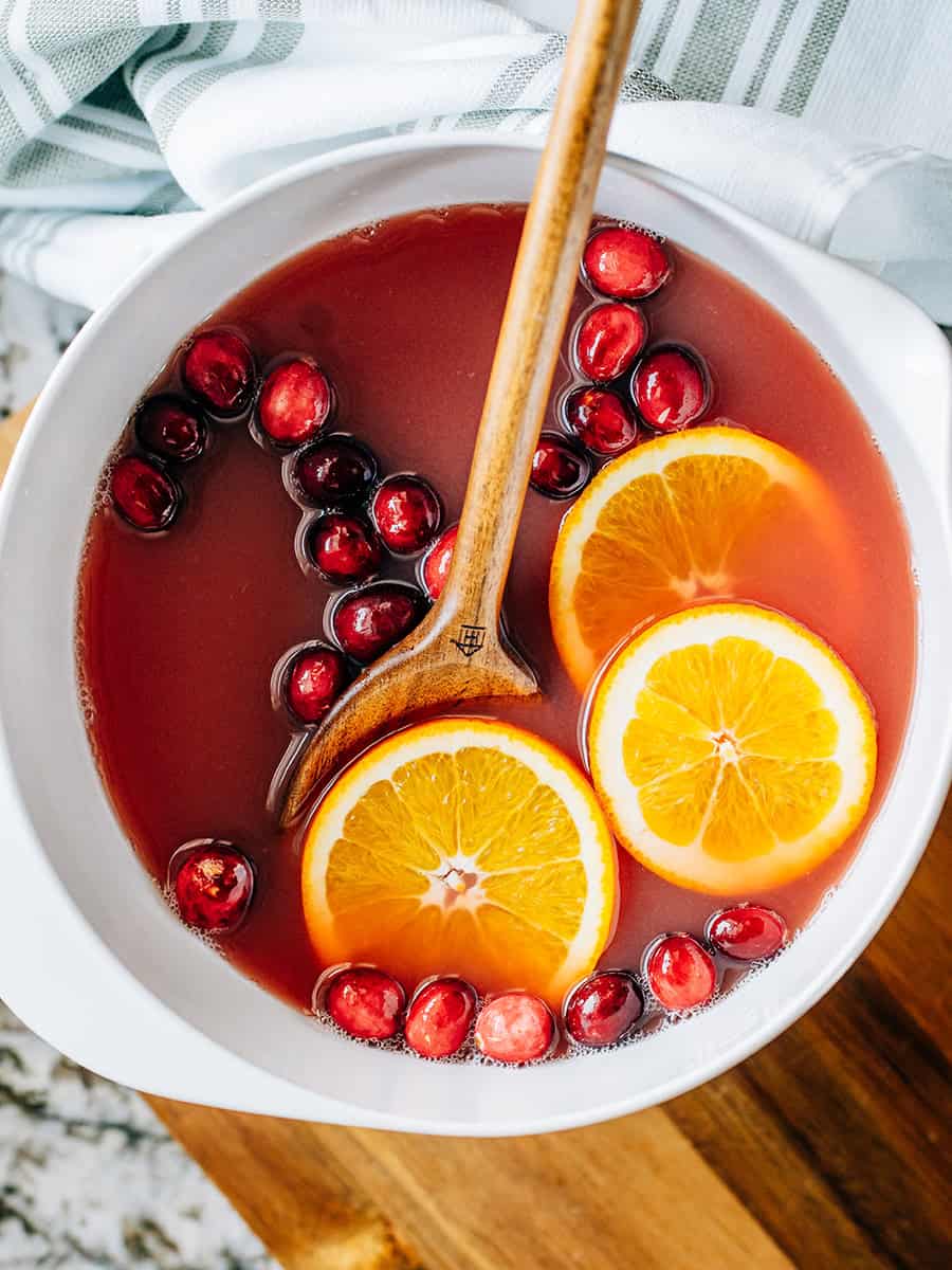 Un bol plein de punch de Noël aux oranges et canneberges garni de canneberges fraîches et de tranches d'orange. Le punch parfait pour les fêtes !