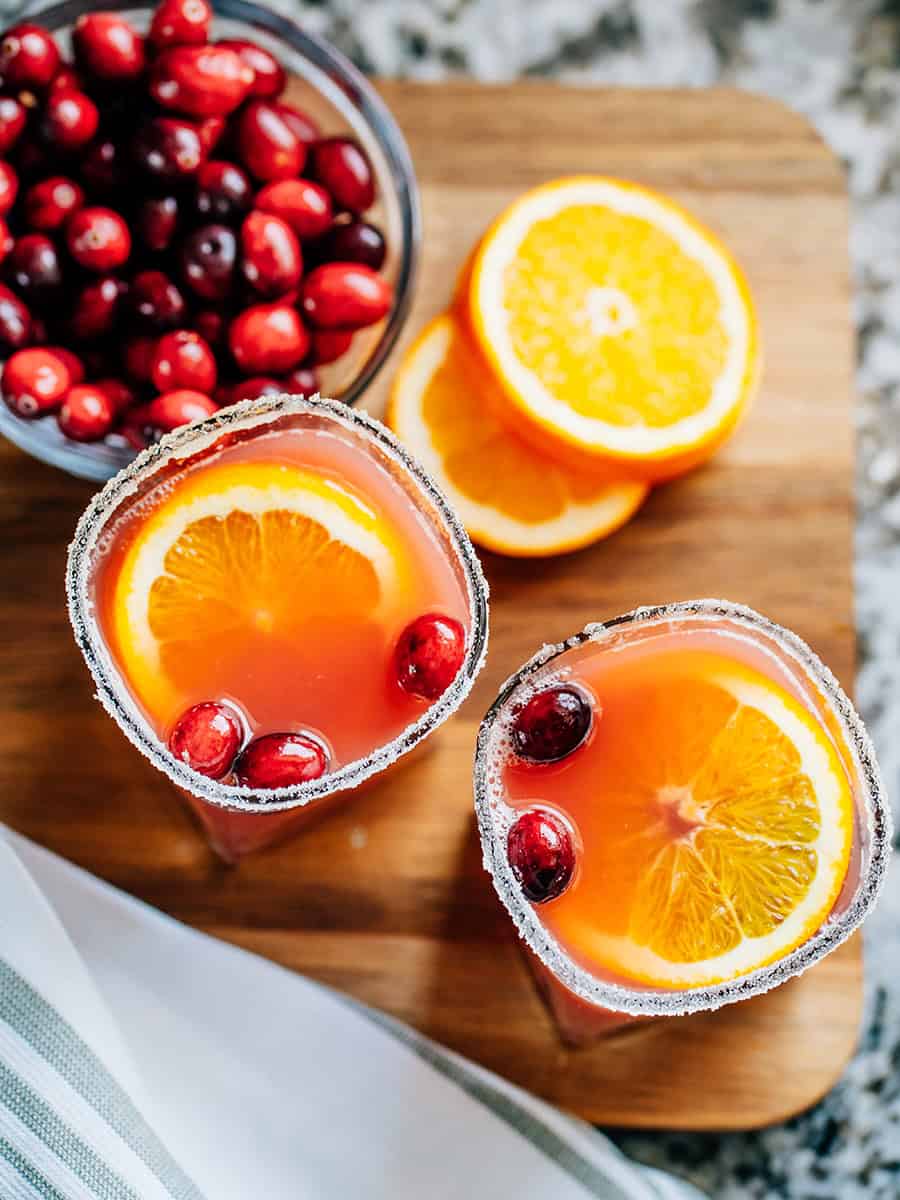 Aperçu : Un verre décoré de sucre rempli de punch de Noël aux oranges et canneberges, garni de canneberges fraîches et de tranches d'orange. Le punch parfait pour les fêtes !