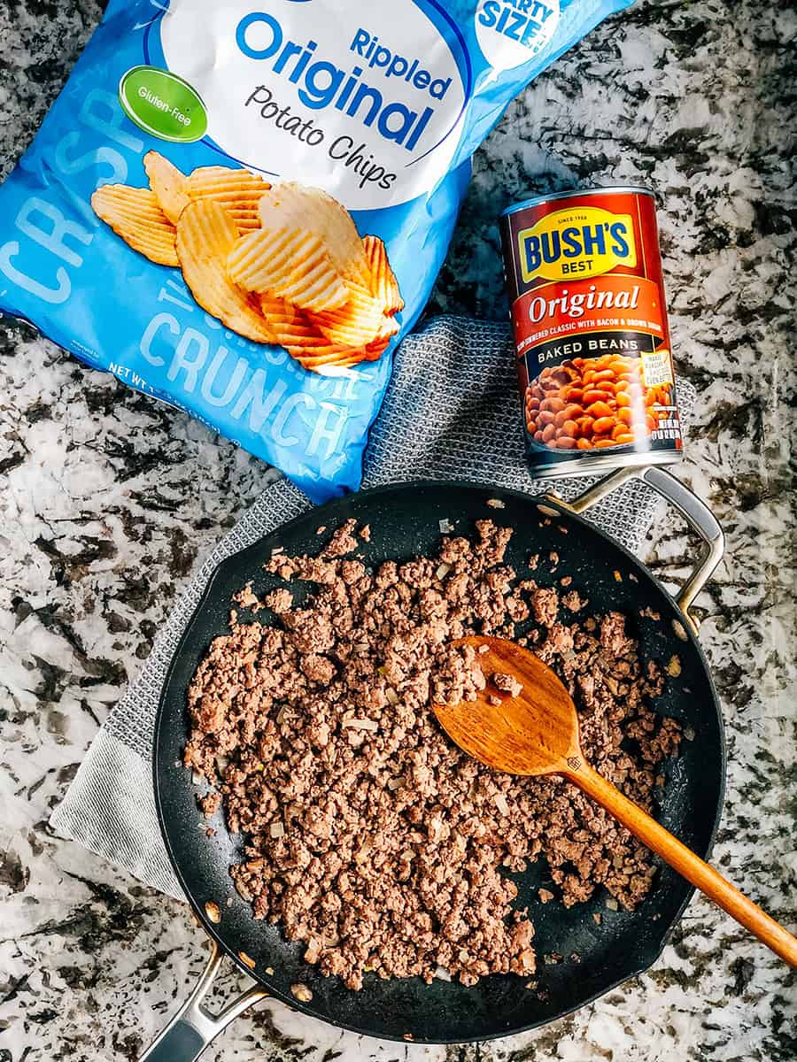 Les trois ingrédients qui composent ce plat simple de viande hachée et de haricots : viande hachée dorée, une grande boîte de haricots au four de Bush et des chips ondulées.