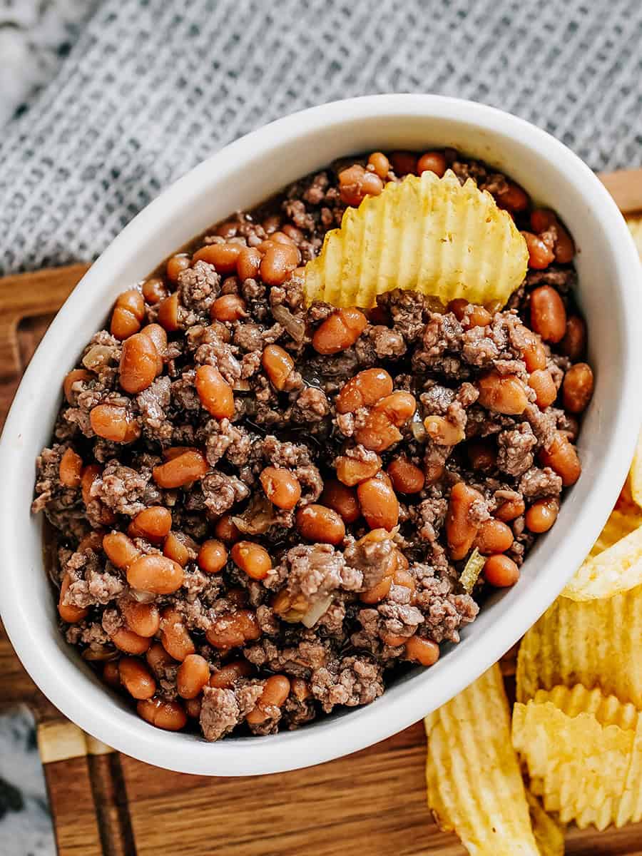 Viande hachée et haricots au four dans un bol avec des chips à côté.