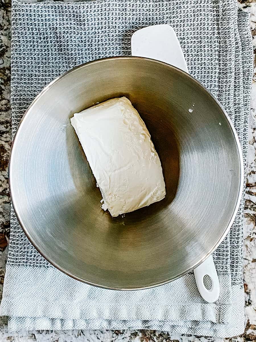 Un bloc de fromage à la crème ramolli dans un bol de mélange.