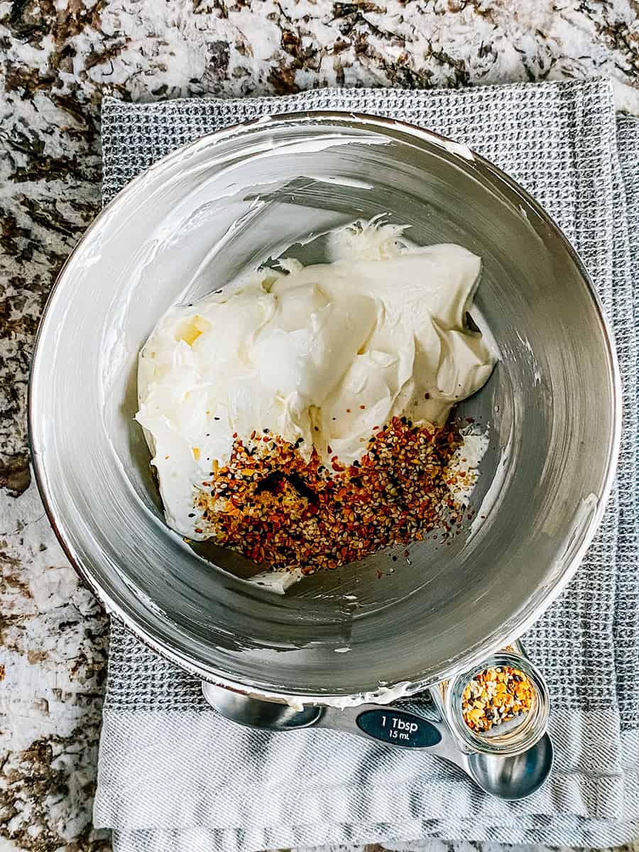 Dans un bol de mélange, fromage à la crème fouetté, crème aigre et épices pour bagels tout en un.