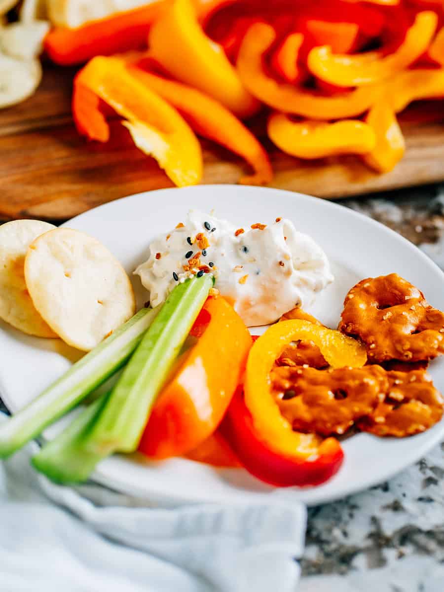 Assiette avec une cuillerée de tartinade de bagel tout en un, croustillants au bretzel, céleri, poivrons et chips pita.