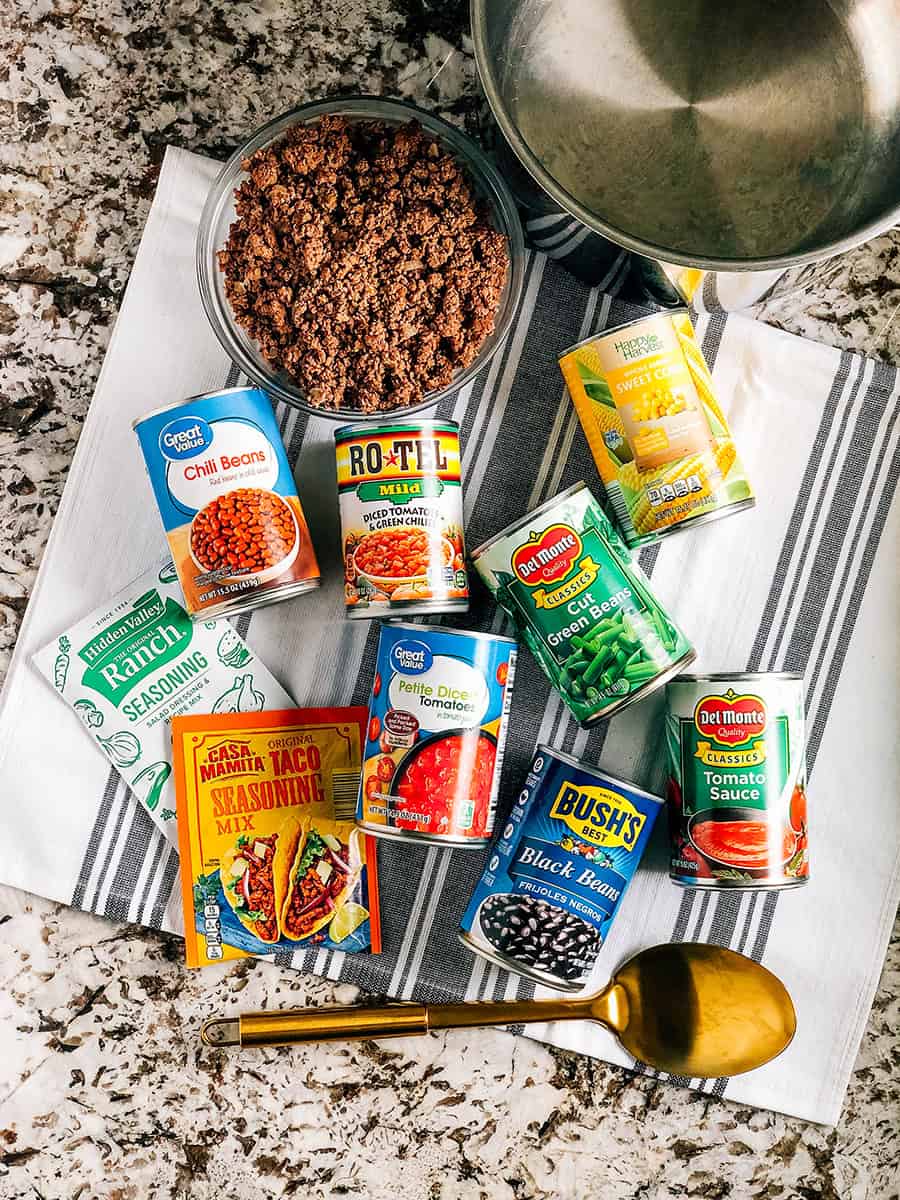 Ingrédients pour la soupe taco à 7 boîtes : maïs en conserve, haricots verts, Rotel, tomates en dés, sauce tomate, haricots chili, haricots noirs, boeuf haché doré savoureux, Ranch et assaisonnements taco. La soupe est garnie d'une cuillerée de crème aigre, de fromage cheddar râpé et de chips de tortilla écrasées.