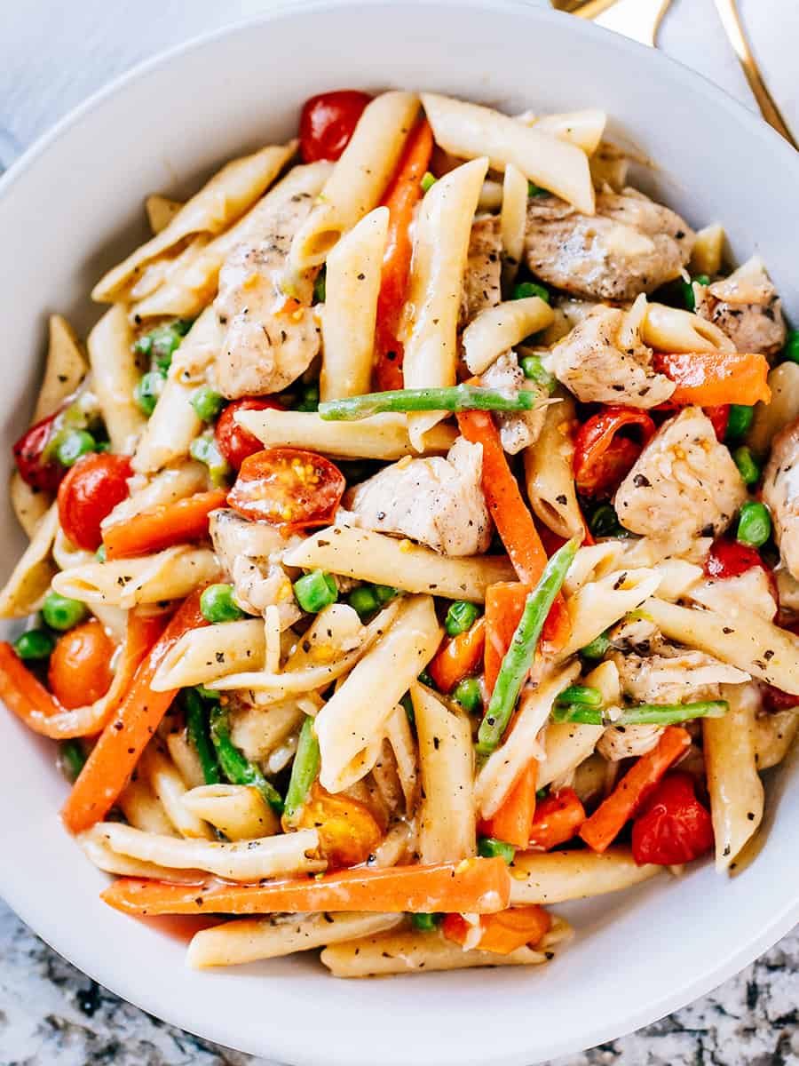 Vue d'ensemble du poulet primavera servi, plein de légumes de printemps, de pâtes penne et de poitrines de poulet frites.