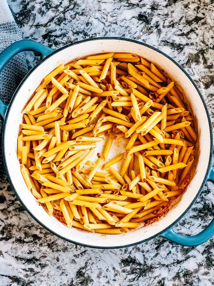 Pâtes penne dans la sauce d'huile et de beurre provenant de la friture des morceaux de poulet.