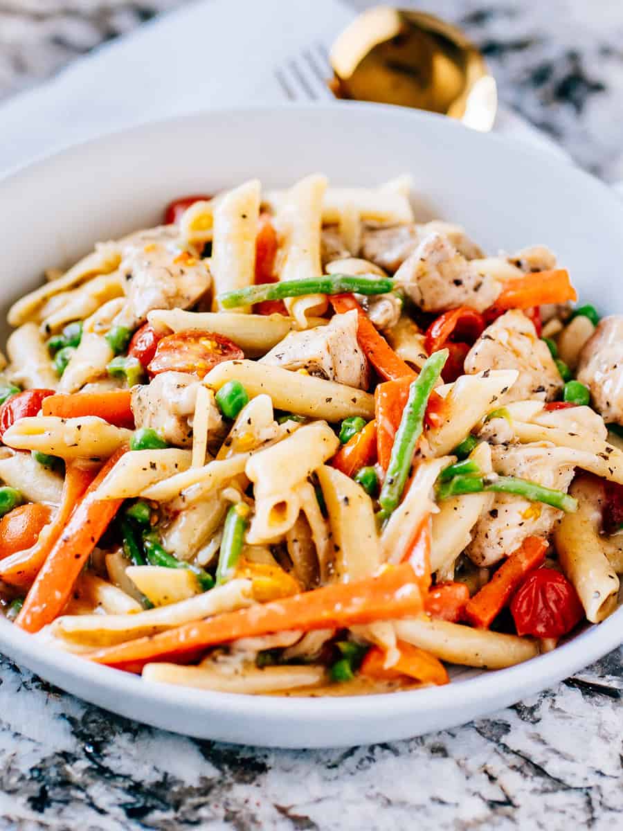 Poulet primavera servi, plein de légumes de printemps, de pâtes penne et de poitrines de poulet frites.