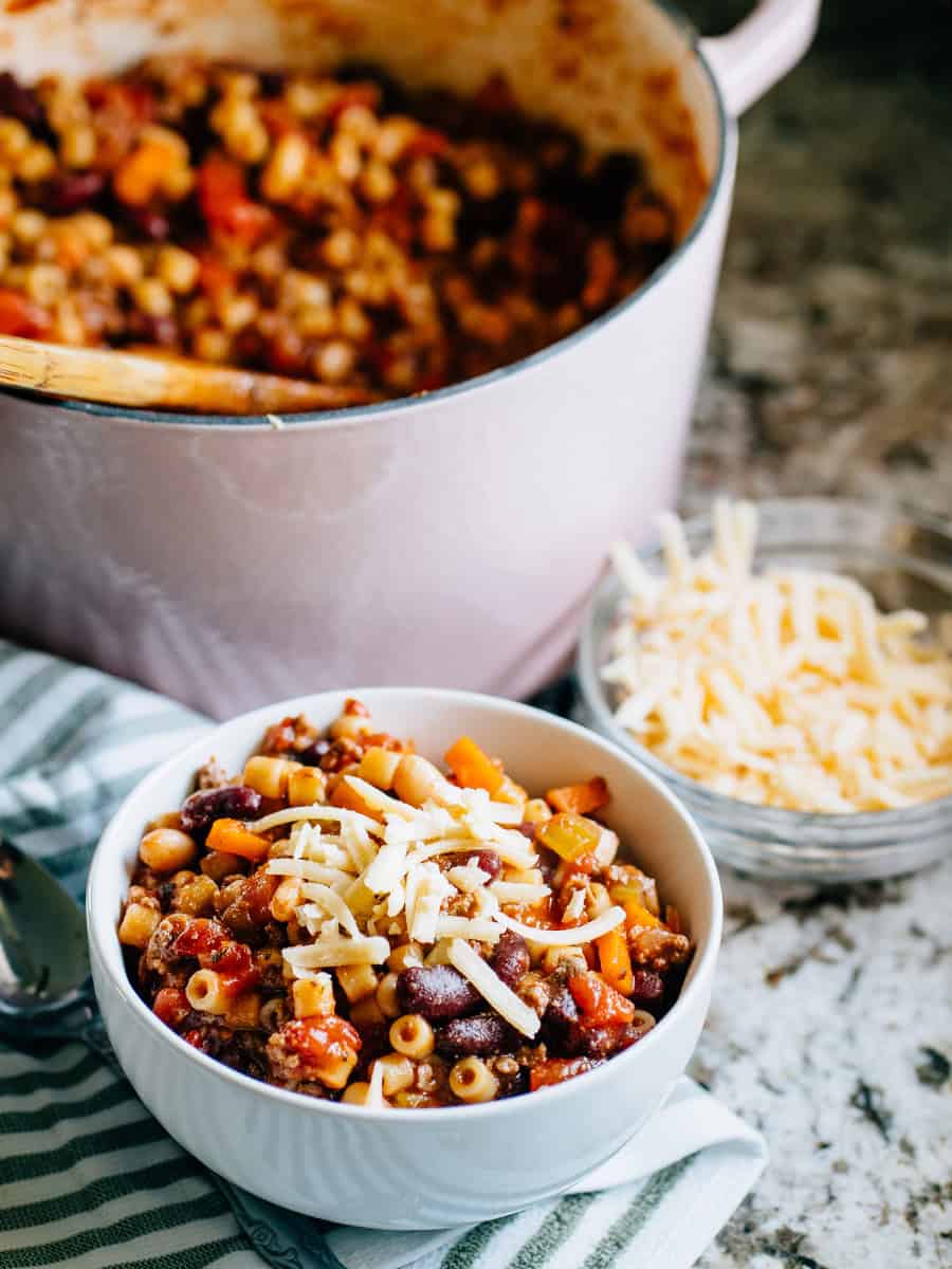 Soupe complète Pasta E Fagioli dans un bol avec une casserole en arrière-plan. C'est une soupe copieuse faite avec de la viande hachée, de délicieux haricots, des légumes tendres et des pâtes Ditalini avec du parmesan fraîchement râpé à côté.