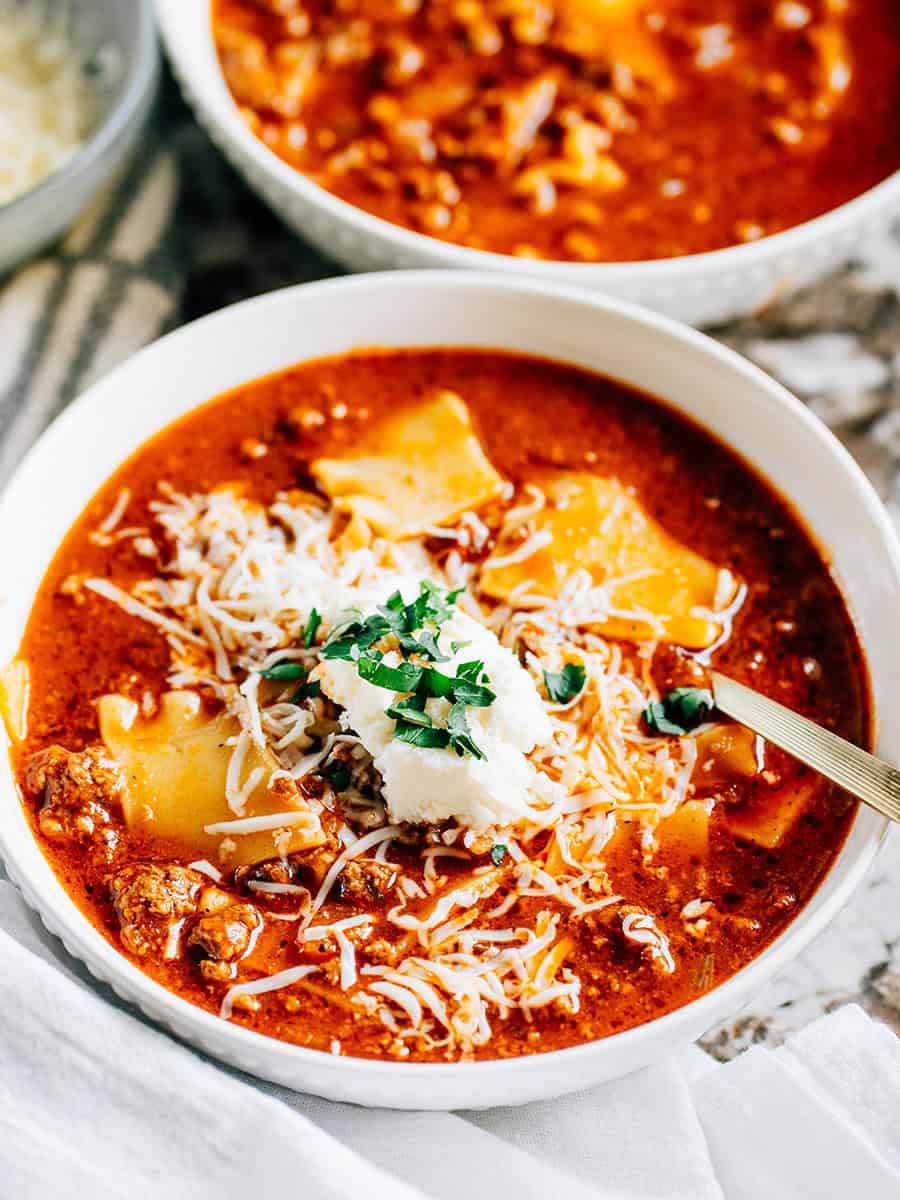 Un bol de soupe de lasagne chaude et réconfortante avec du boeuf dans un bouillon de boeuf et marinara, garni d'une cuillerée de ricotta, de fromage mozzarella râpé et de persil.