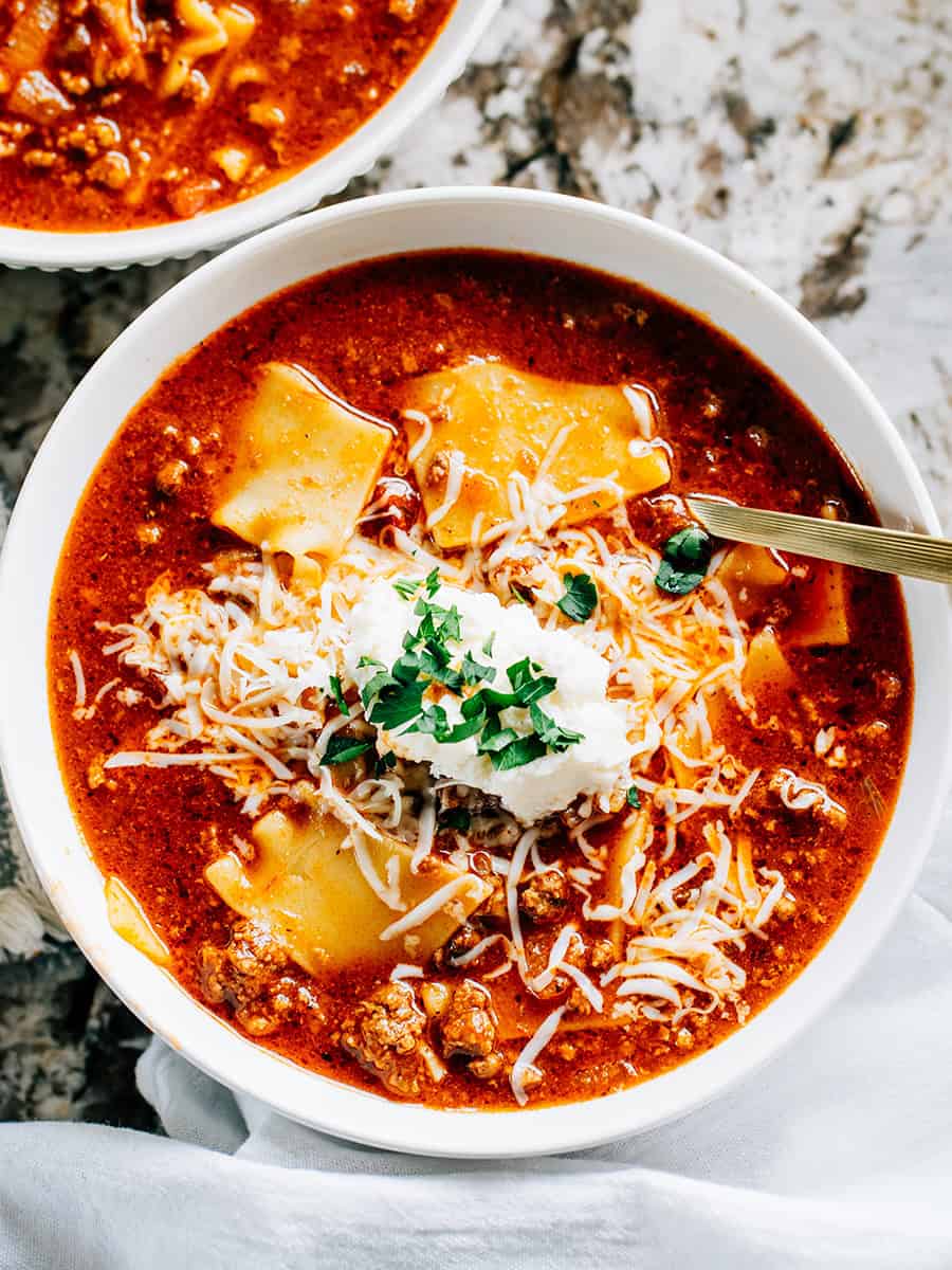 Aperçu : Un bol de soupe de lasagne chaude et réconfortante avec de la viande dans un bouillon de boeuf et marinara, garni d'une cuillerée de ricotta, de fromage cheddar râpé et de persil.