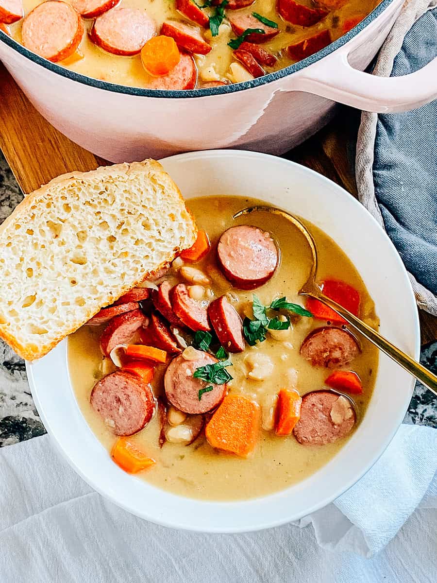 Un bol de kielbasa savoureuse, de carottes cuites tendres et de haricots crémeux Great Northern mijotés à perfection dans une sauce crémeuse avec de l'ail haché et des oignons.