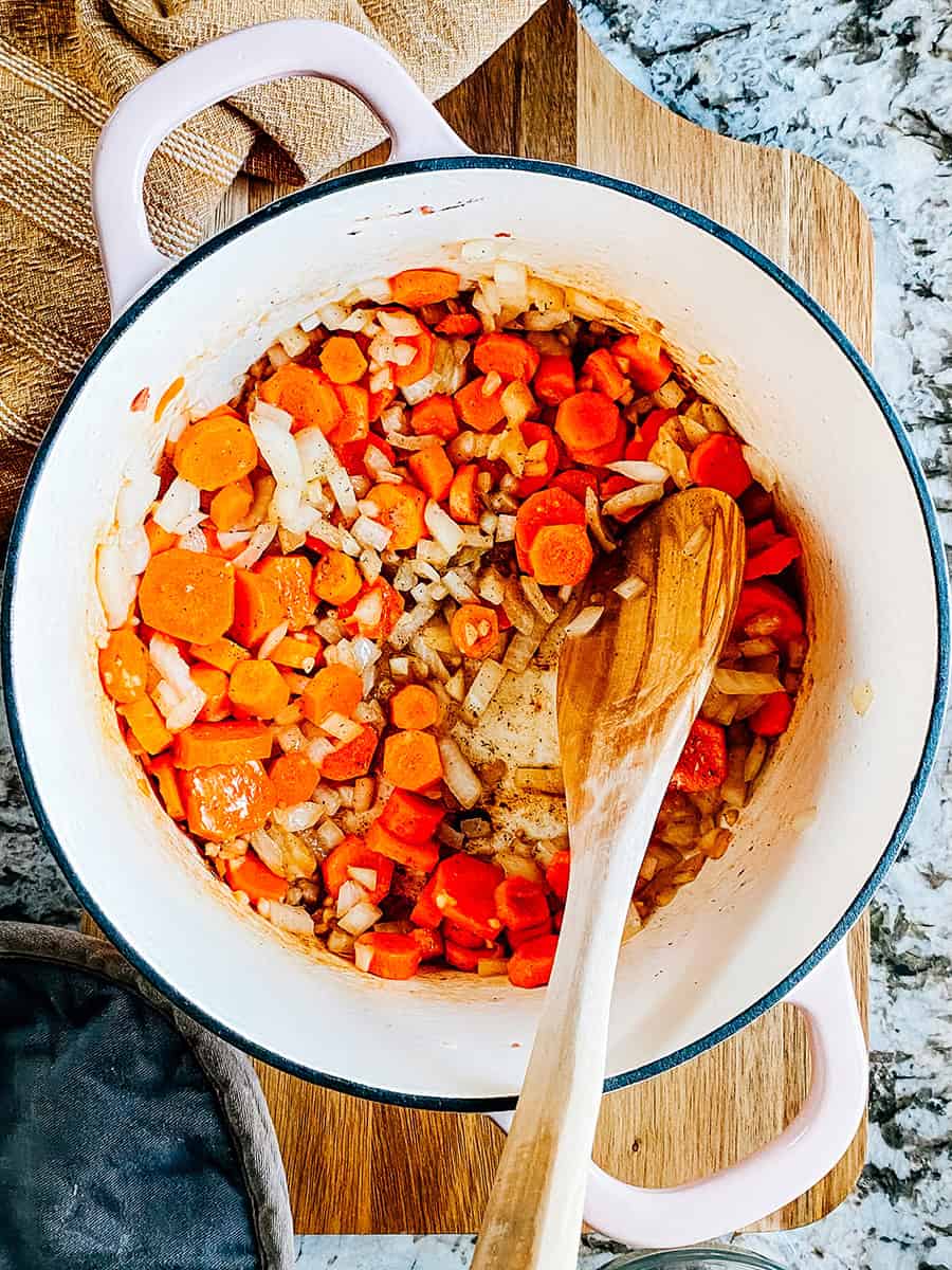 Étape quatre : Beurre fondu, ail haché, carottes coupées et oignons hachés dans une casserole. Mélangés pour combiner puis cuire.