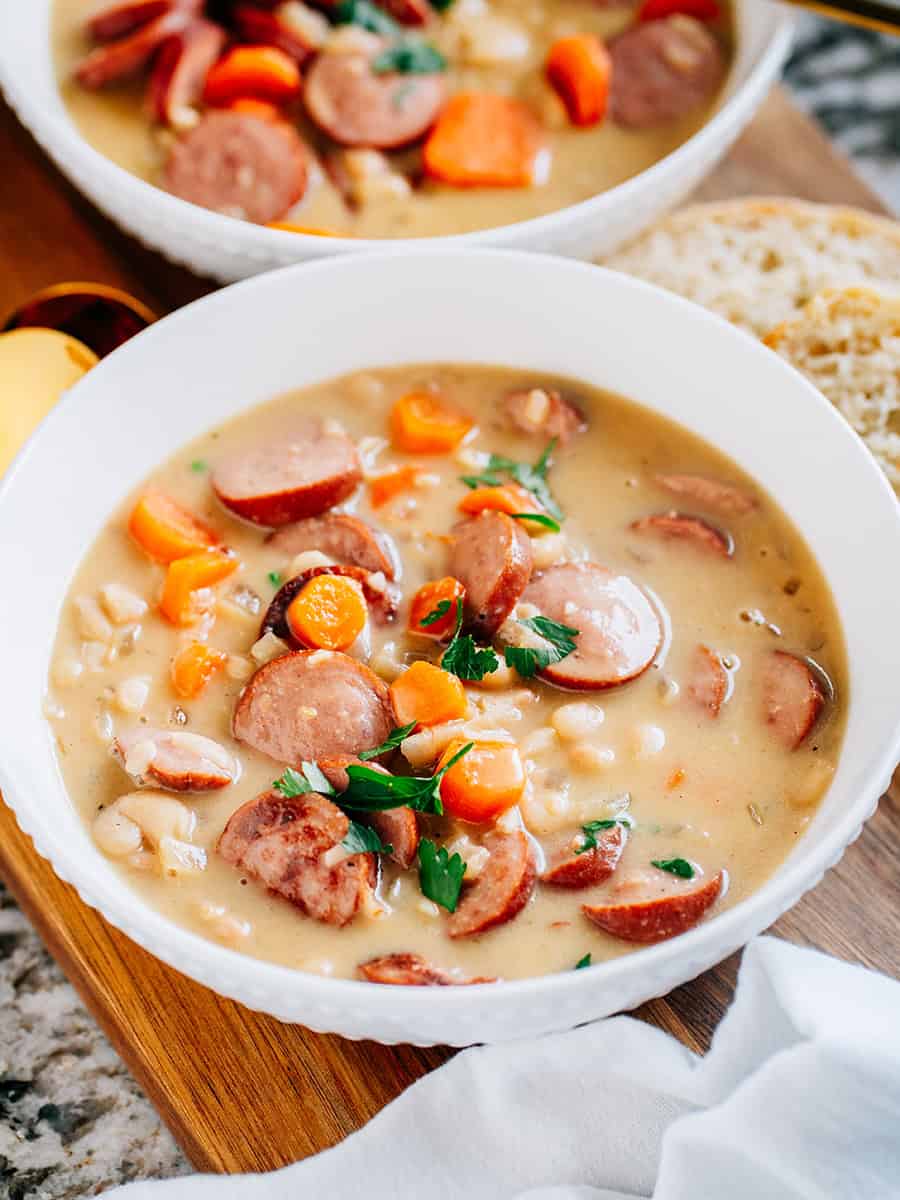 Deux bols de kielbasa savoureuse, de carottes cuites tendres et de haricots crémeux Great Northern mijotés à perfection dans une sauce crémeuse avec de l'ail haché et des oignons. La soupe parfaite pour un hiver en semaine !