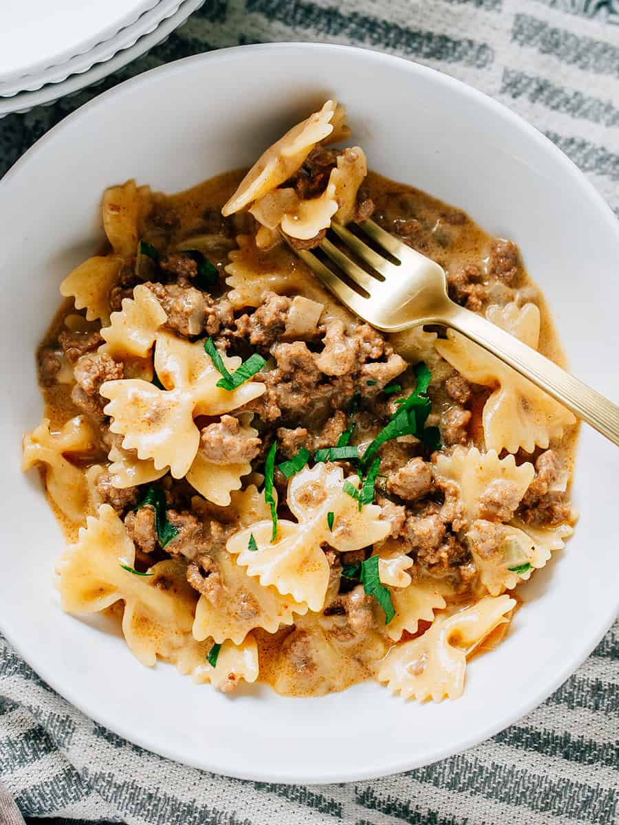 Gros plan : Un plat copieux de boeuf et de pâtes en forme de nœud papillon dans une sauce crémeuse avec du fromage cheddar fondu ! Des pâtes également sur la fourchette.