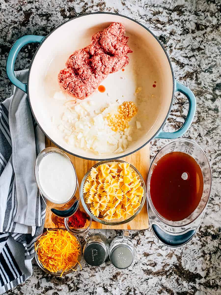 Ingrédients pour les Pâtes en Nœud Papillon et Boeuf Haché Crémeux : boeuf haché, oignon en dés, ail émincé, sel, poivre, paprika, crème épaisse, bouillon de boeuf, pâtes en nœud papillon, et fromage cheddar râpé.