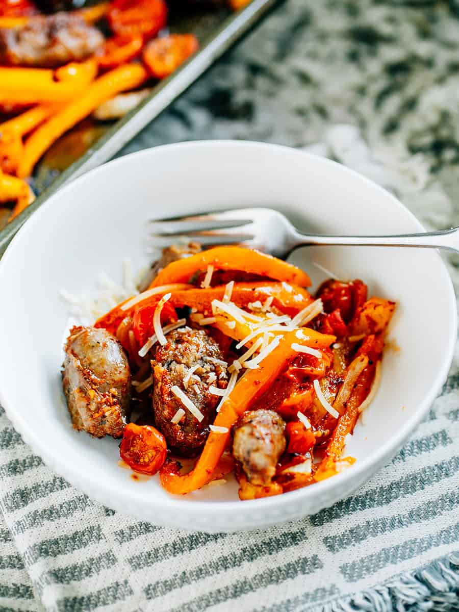 A bowl do this easy sheet pan sausage and peppers recipe in a bowl with freshly grated parmesan cheese sprinkled on top.