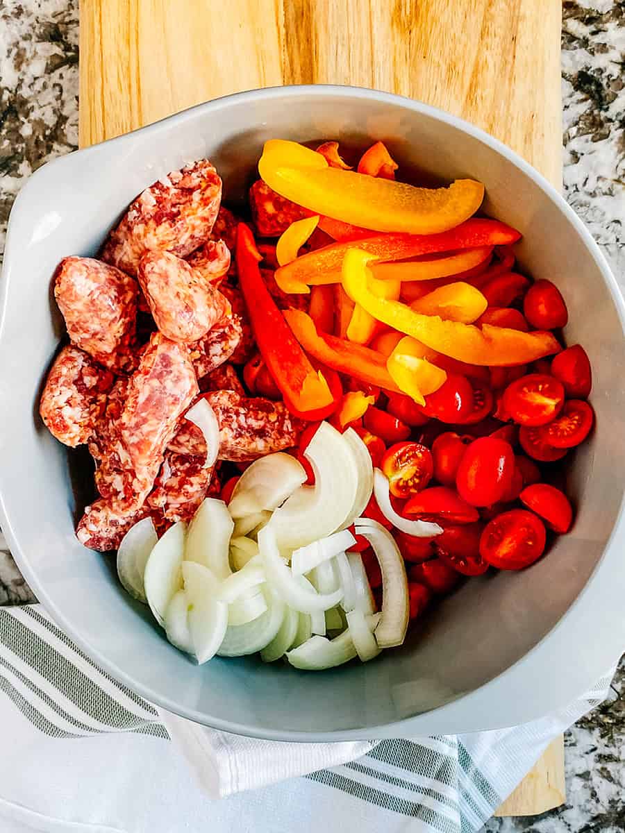 Cut up sweet Italian sausage, onions, bell peppers, and cherry tomatoes in a large bowl.