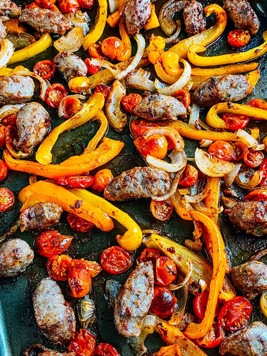 Close up: Freshly baked and delicious sausage and peppers on a rimmed baking sheet.