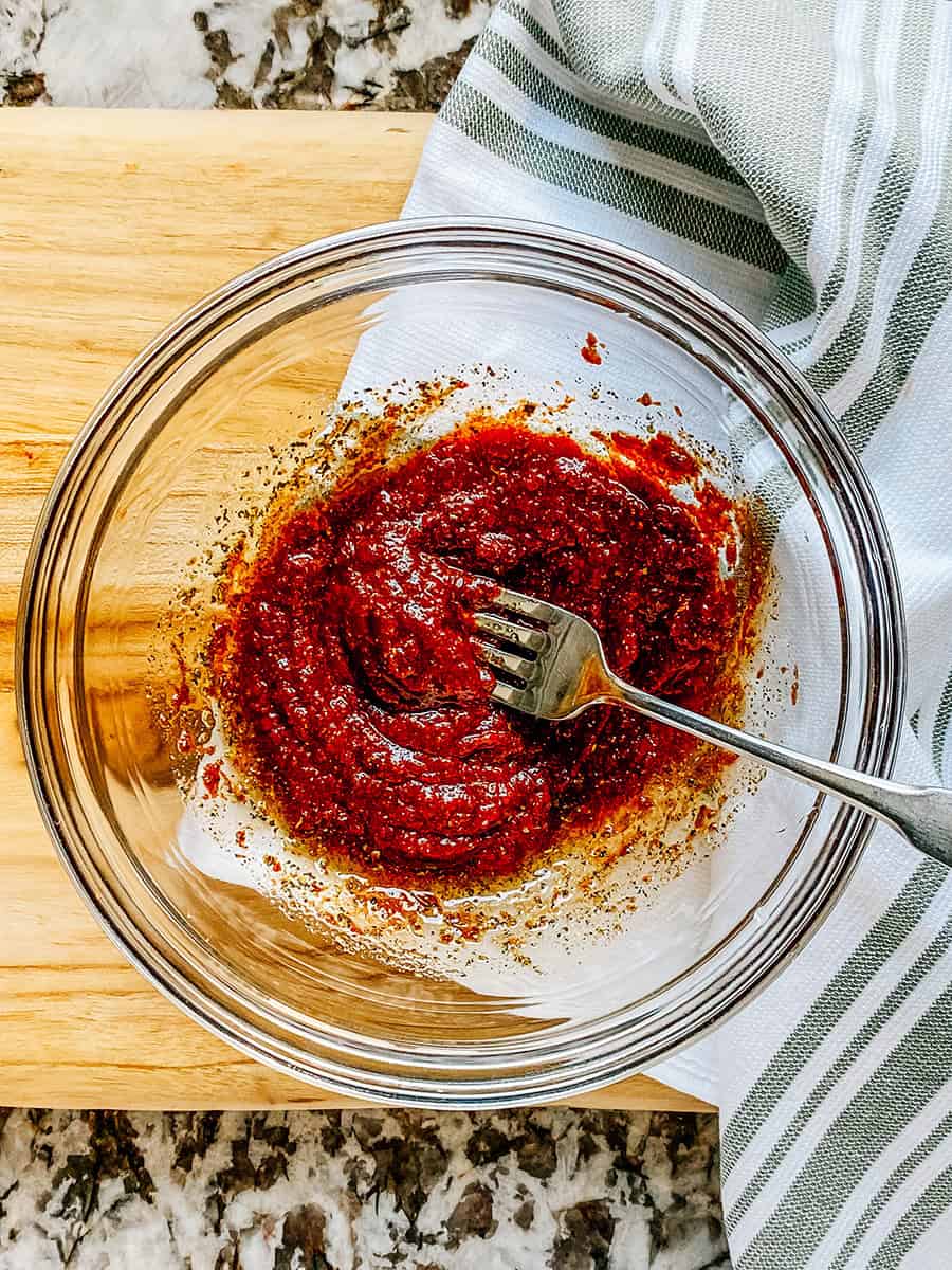 Whisked tomato paste, balsamic vinegar, oil, and seasonings in a glass bowl.