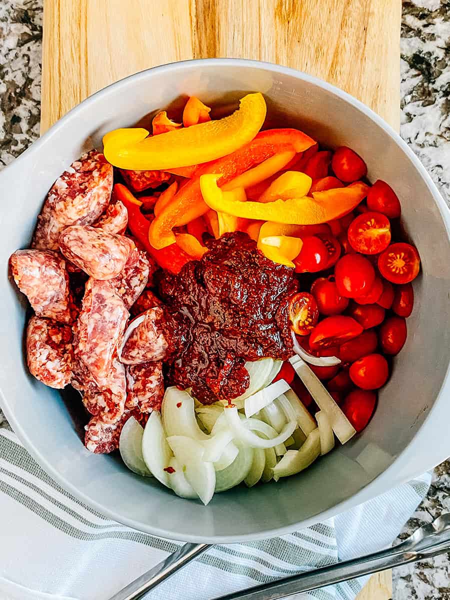 Cut up vegetables and sausage in a bowl with the marinade on top.