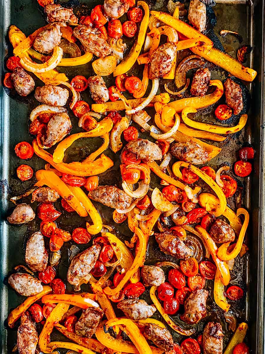 Freshly baked sausage and peppers on a rimmed baking sheet.