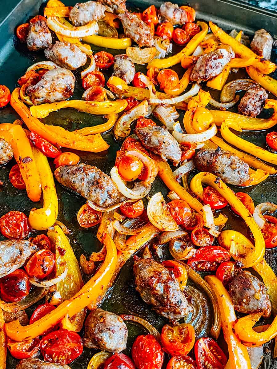 Different angle: Freshly baked and delicious sausage and peppers on a rimmed baking sheet.